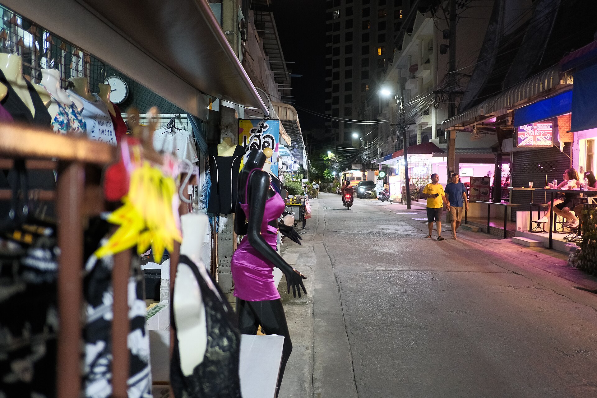 DSCF1208 A quiet neon lit street at night with storefront mannequins and a few people and scooters passing by